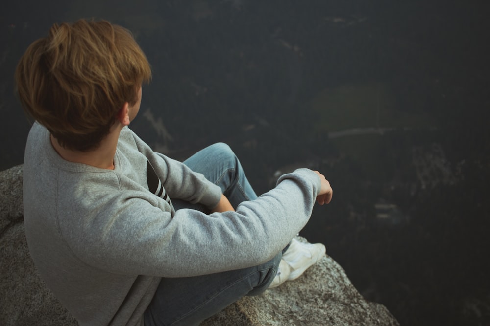 man sitting on rock near cliff