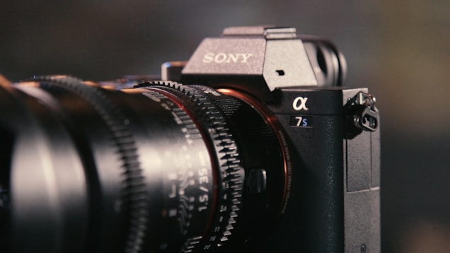 A close-up view of a Sony Alpha 7S camera, focusing on the intricate details of the lens and body. The branded logo is visible, and the camera's design features a combination of sleek textures and precise engineering.
