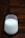 A glass of milk is placed on a wooden surface. The background consists of a dark wooden texture with defined lines and patterns. The milk in the glass appears to be fresh, with small bubbles visible on the top layer.