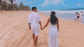 Couple walking hand in hand on a white sandy beach with palm trees swaying in the breeze