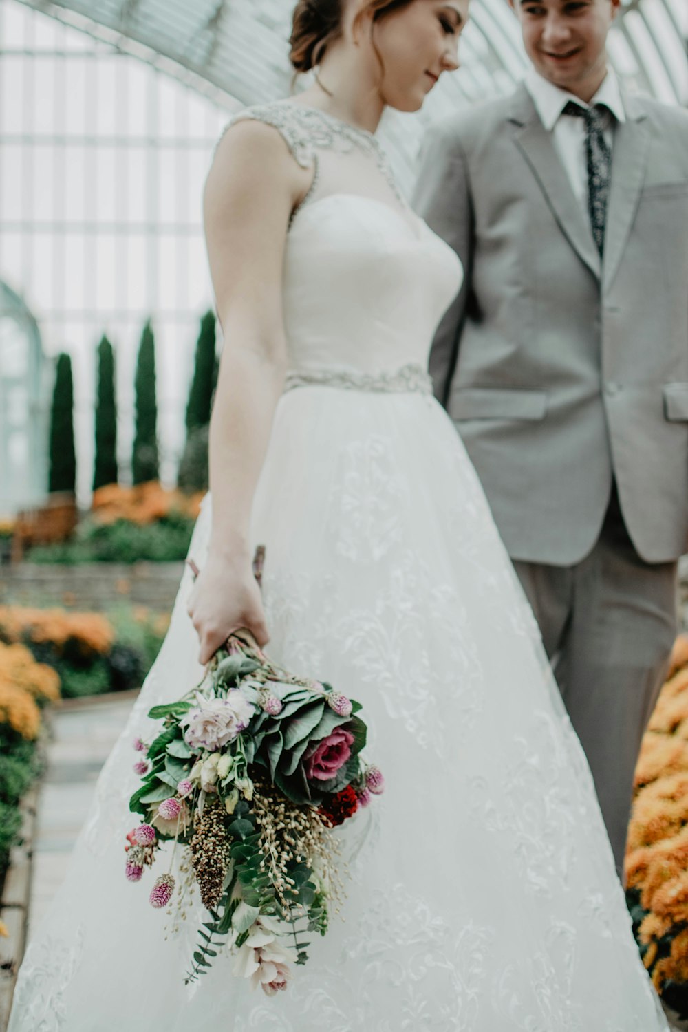 Braut geht mit Bräutigam am Gang und hält Blumenboquet