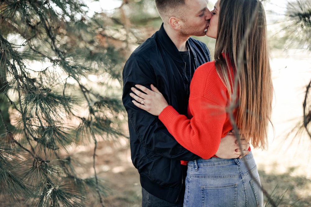 casal se beijando ao lado de árvores de folhas verdes durante o dia
