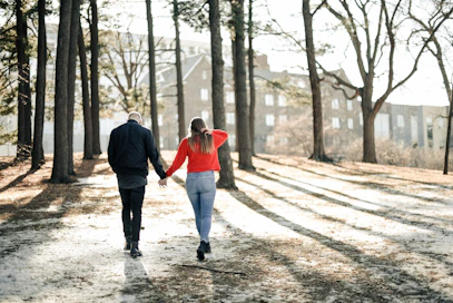 couple holding hands while walking near brown trees during daytime