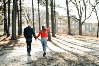 couple holding hands while walking near brown trees during daytime