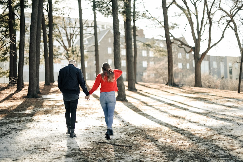 couple holding hands while walking near brown trees during daytime