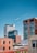 A series of modern and industrial buildings against a clear blue sky. The structures vary in architectural style, featuring brick exteriors and glass windows. The scene conveys an urban atmosphere with a mix of historical and contemporary designs.