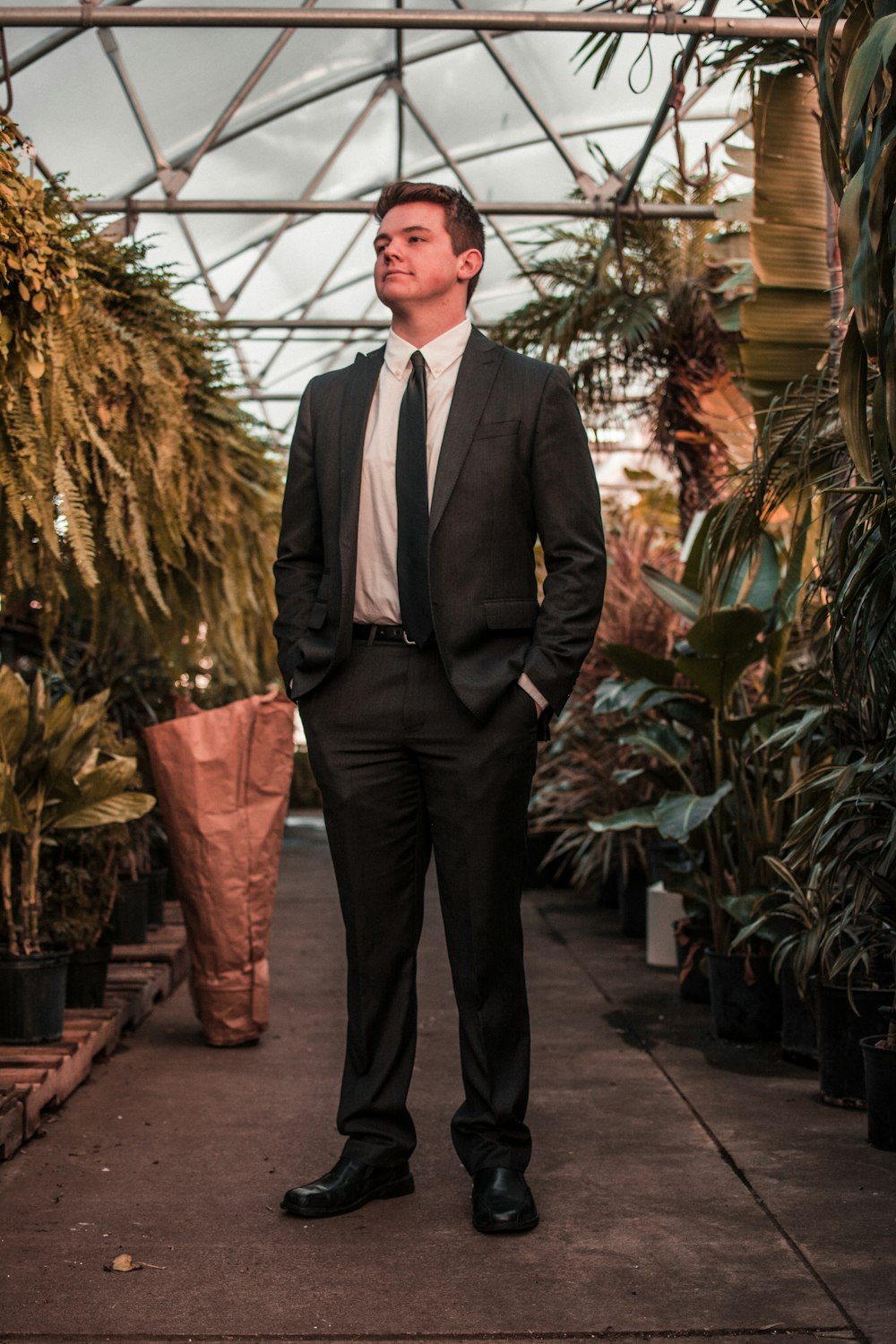 man wearing suit jacket standing between the plants