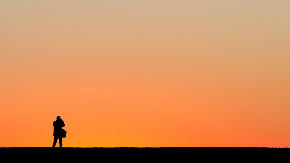 silhouette of standing person under orange sky