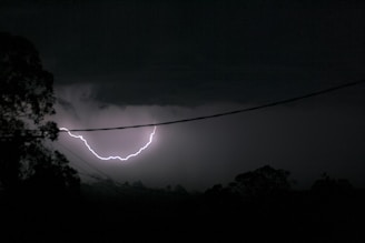 A powerful lightning flash illuminating a rural landscape with silhouetted trees.