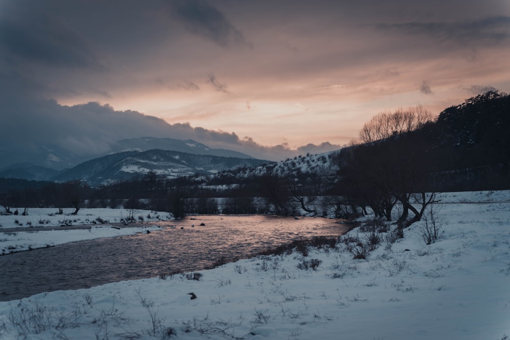 mountains by the water near snow covered land during sunset