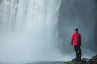 man standing on a rock facing waterfalls thoughtful zoom background