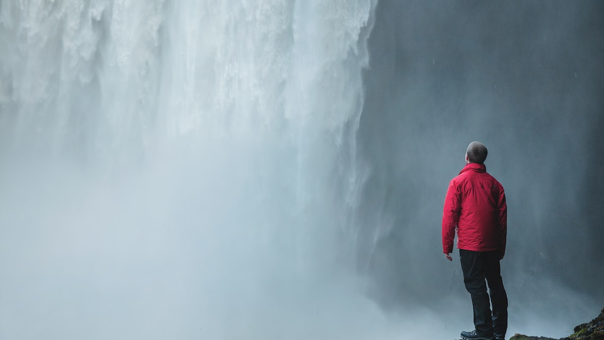 man standing on a rock facing waterfalls