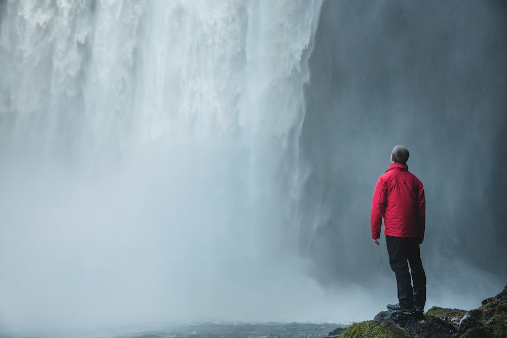 man standing on a rock facing waterfalls