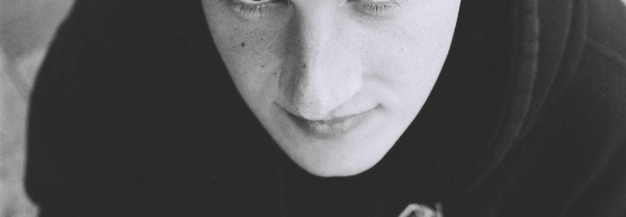 A young person gazes upward while holding a cup. They are wearing a black cap with the word 'YOUTH' on it and a dark hoodie. The image is in black and white, contributing to a nostalgic or contemplative atmosphere.