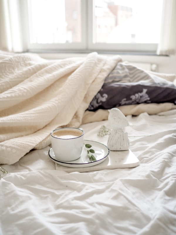 Latte sitting on a white plate on a bed with white sheets