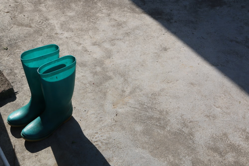 pair of green rain boots on gray pavement