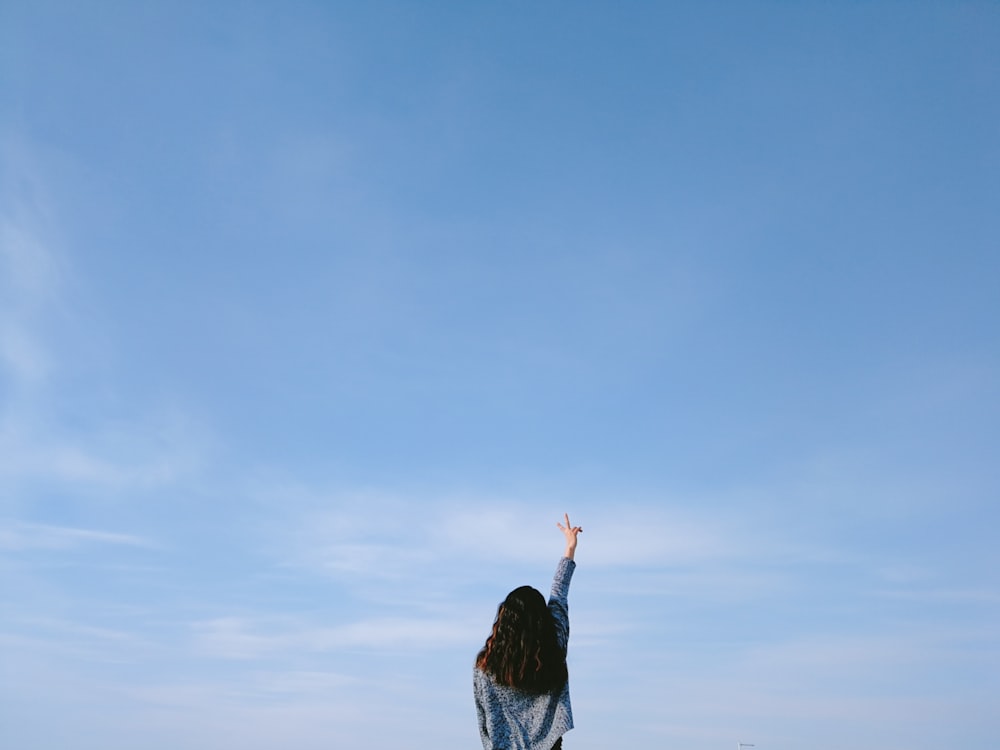 woman in gray top performing peace sign under blue sky