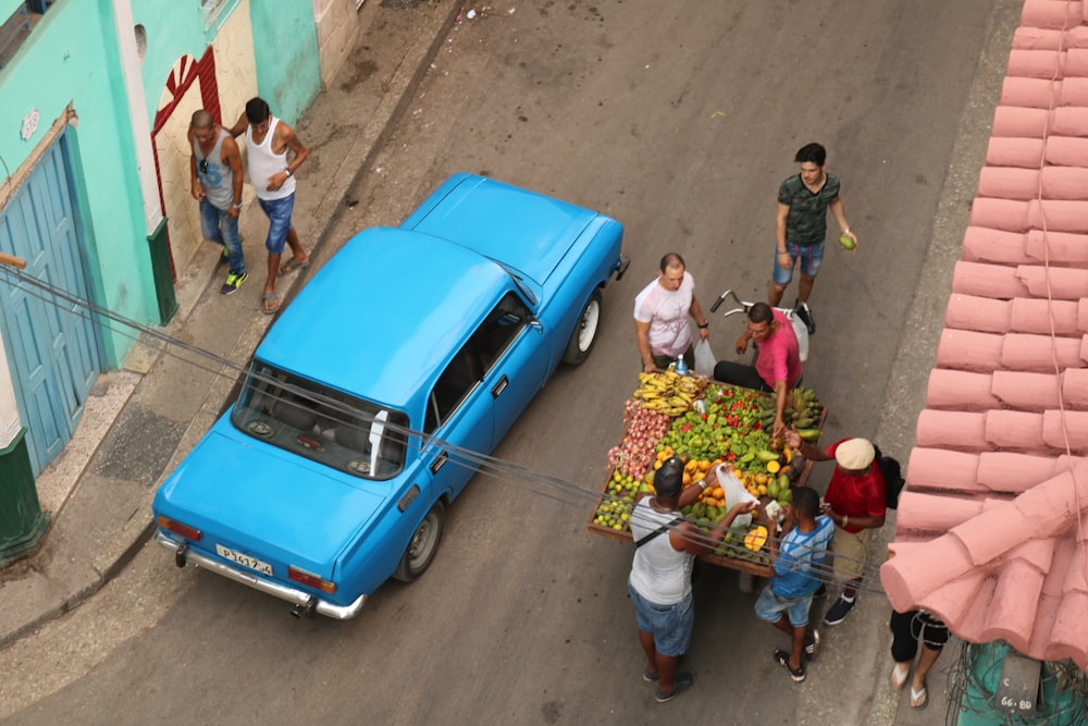 sedan crossing road beside fruit vendor cart