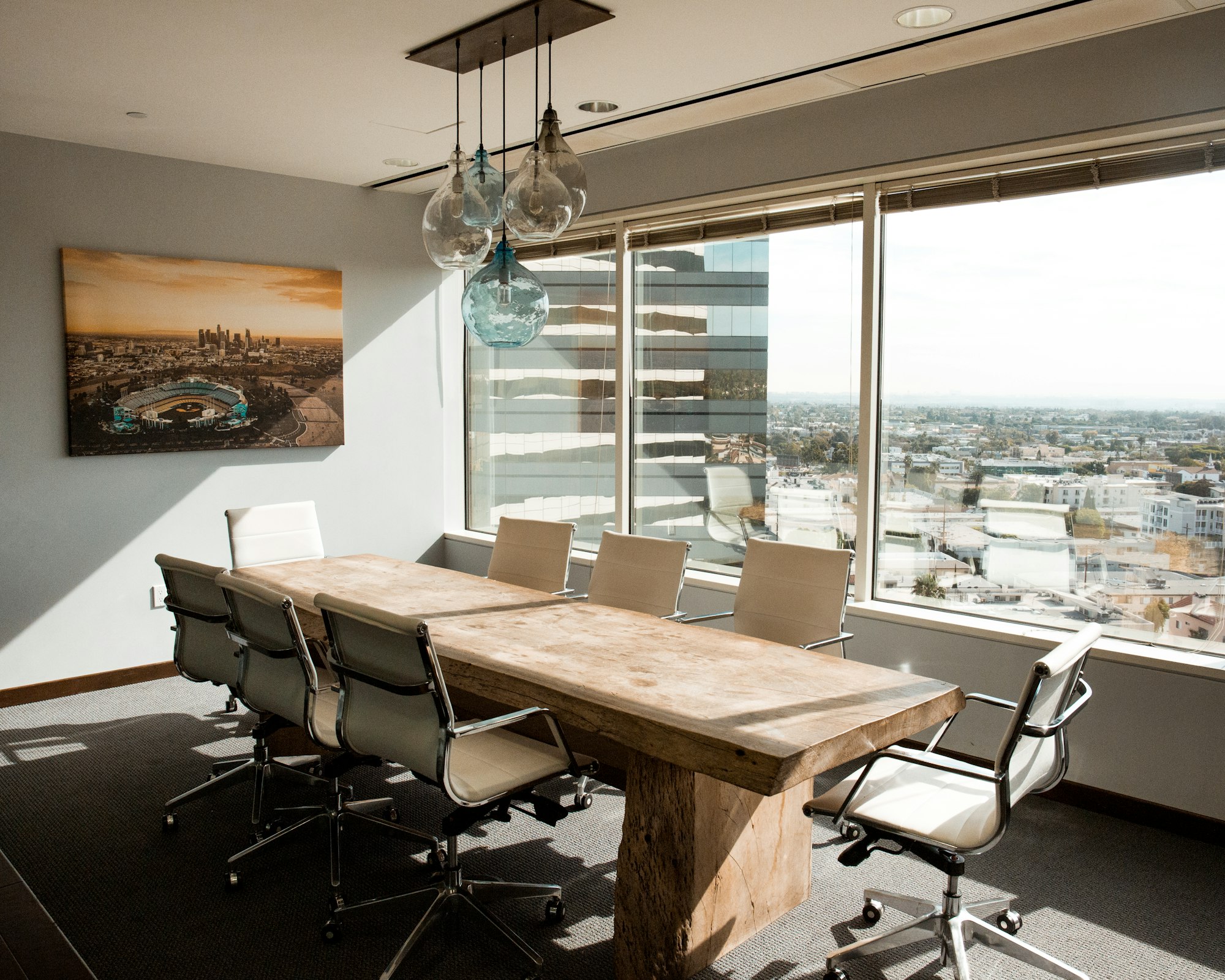 A corporate board room table with 8 chairs, a view over a city in the background, and a photo on the wall.