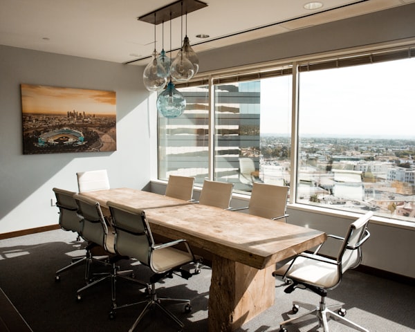 A corporate board room table with 8 chairs, a view over a city in the background, and a photo on the wall.