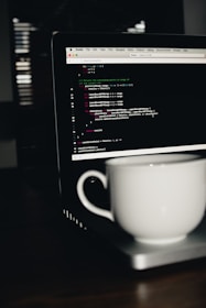 photo of white ceramic teacup on turned on MacBook Pro