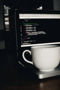 photo of white ceramic teacup on turned on MacBook Pro