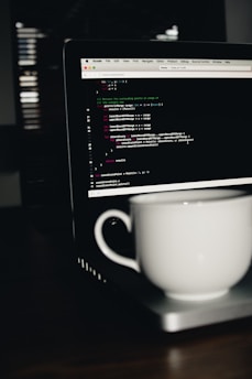 photo of white ceramic teacup on turned on MacBook Pro