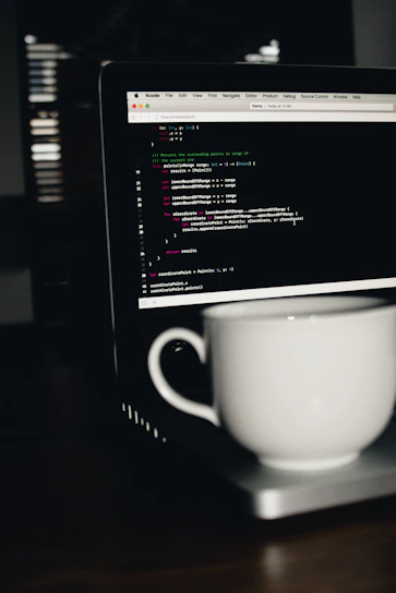 photo of white ceramic teacup on turned on MacBook Pro