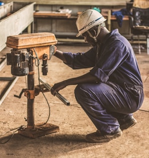 man wearing white hard hat operating brown drill press