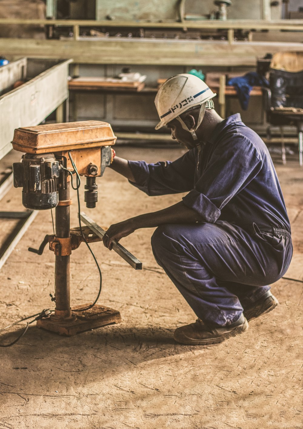 man wearing white hard hat operating brown drill press