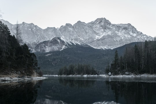 rocky mountain filled with snow near body of water under white sky in Eibsee Germany