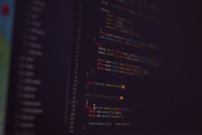 A dark background with colorful lines of code in various programming languages displayed on a screen. The text includes snippets of functions and logical statements.
