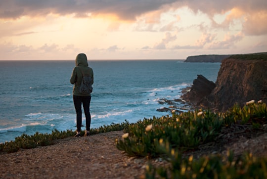 person on mountain beside body of water in Zambujeira do Mar Portugal