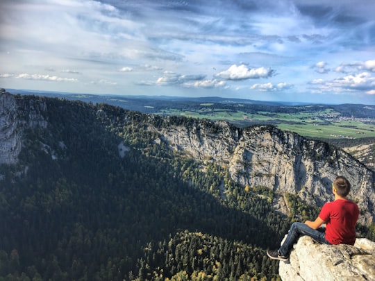 man sitting on brown rock during daytime in Creux du Van Switzerland