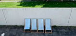 Stacked patio chairs neatly arranged beside a sunlit garden wall.