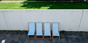 A stack of colorful patio chairs arranged neatly on a sunlit terrace with greenery in the background