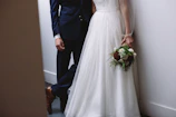 A stylish couple posing in front of a minimalist white modular backdrop at a wedding.