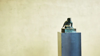 A vintage miniature sculpture from the 1950s displayed on a simple wooden stand.