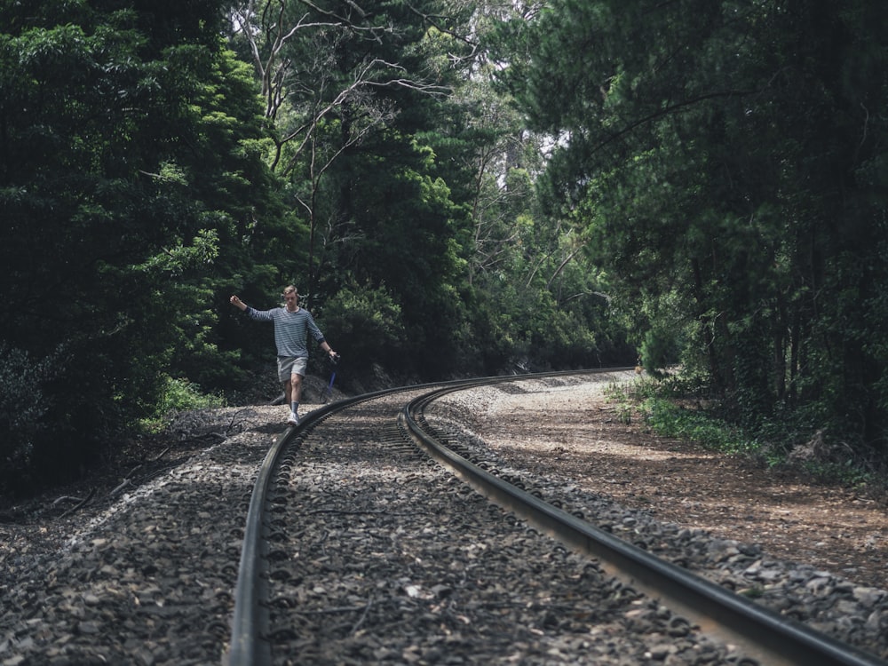 person walking through train rails between forest during daytime