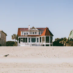 A cozy southern-style home with a wraparound porch overlooking a sandy beach.