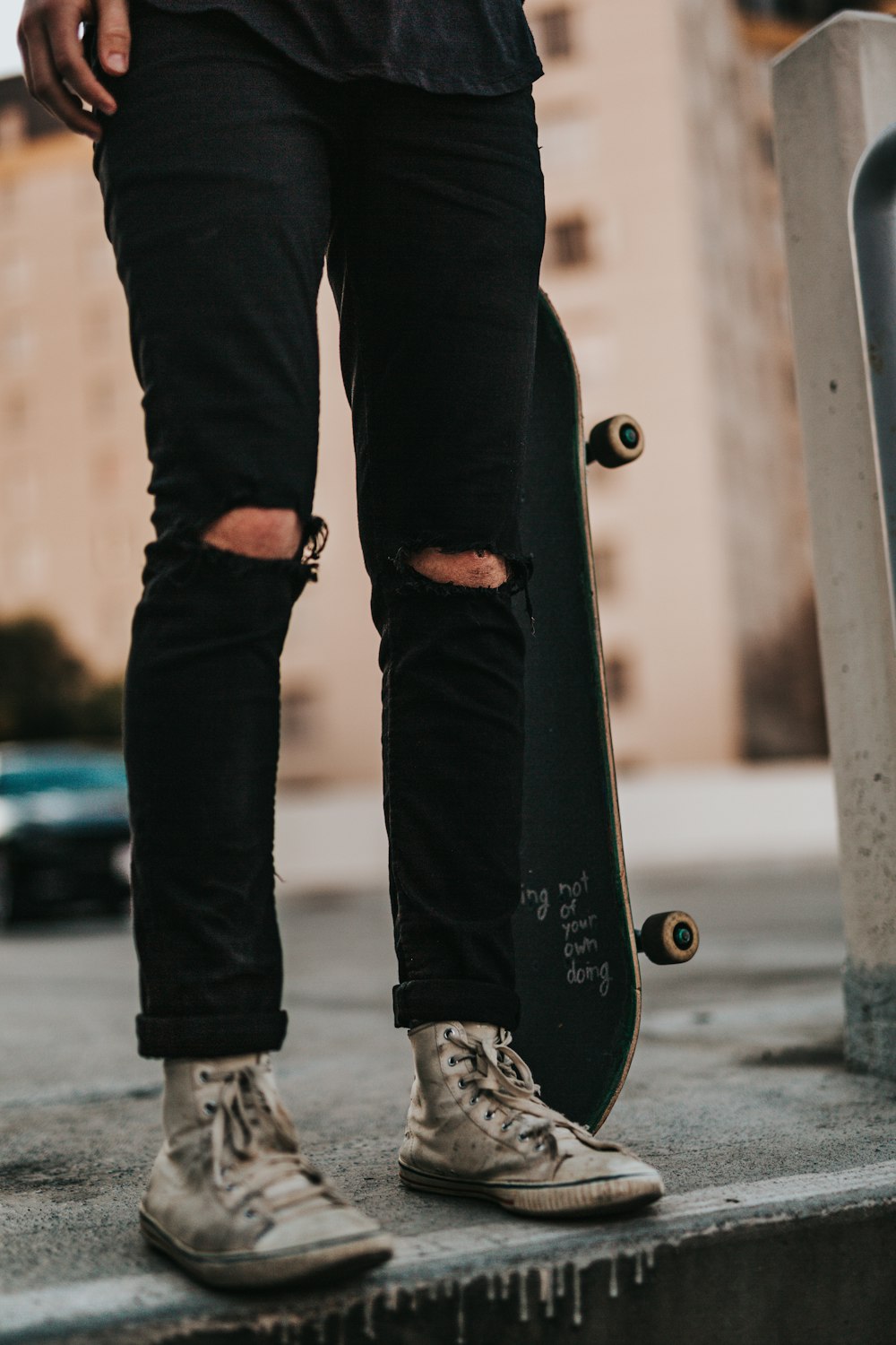 Persona que usa pantalones de mezclilla negros mientras sostiene una patineta