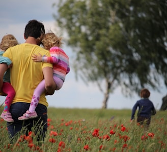 man carrying to girls on field of red petaled flower