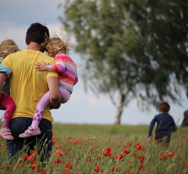 man carrying to girls on field of red petaled flower