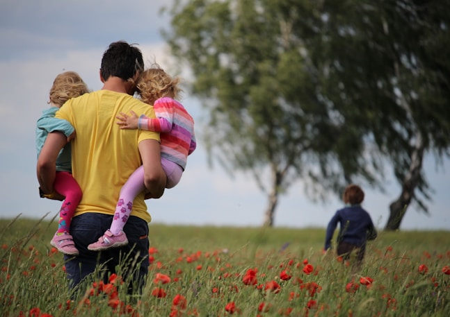 man carrying to girls on field of red petaled flower