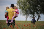 man carrying to girls on field of red petaled flower