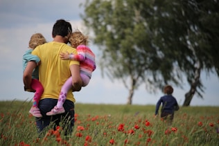 man carrying to girls on field of red petaled flower