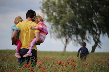 man carrying to girls on field of red petaled flower