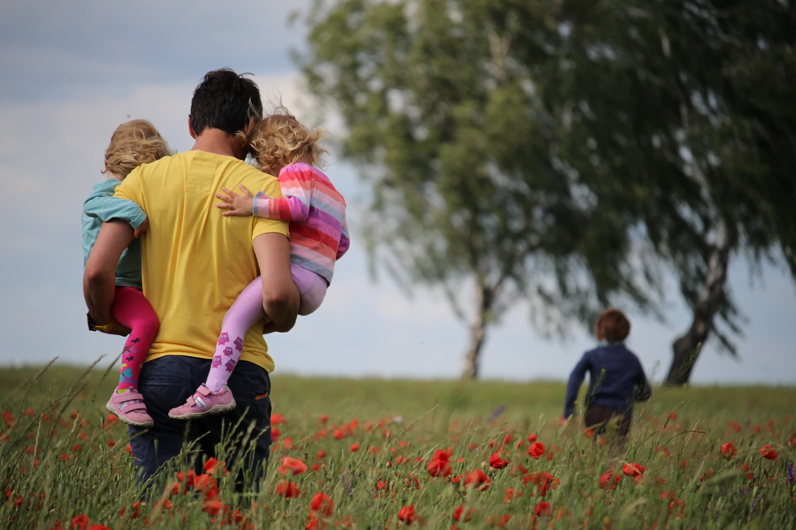 A father carrying his two young children through a sunlit field