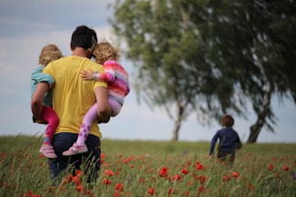 man carrying to girls on field of red petaled flower