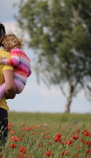 man carrying to girls on field of red petaled flower